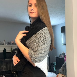 May include: A woman wearing a black, gray, and white crocheted shawl. The shawl has a triangular shape and is made with a variety of stitches.