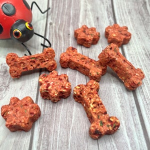 May include: A variety of dog treats in the shapes of bones and stars. The treats are a reddish-brown color and have a speckled appearance.