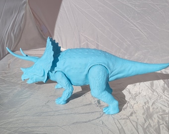 May include: A light blue plastic triceratops dinosaur toy. The toy has three horns, a frill, and a long tail. The dinosaur is standing on four legs and has a detailed texture. The toy is approximately 18 inches long.
