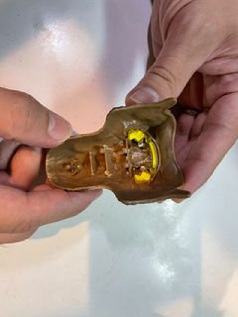 May include: A brown plastic mold with a yellow resin cast inside. The mold is open and the resin cast is visible. The resin cast is shaped like a human head with a detailed face.