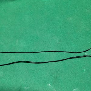 May include: Two black cords are lying on a green surface. The cords are parallel to each other and are about the same length.