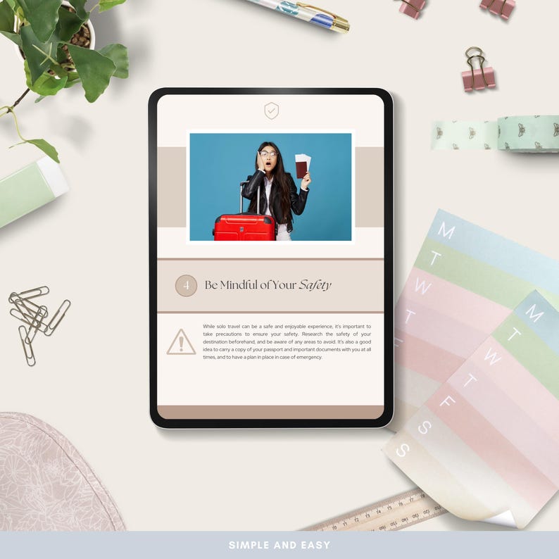 May include: A digital tablet displays a travel safety guide with the text "Be Mindful of Your Safety." The guide features an image of a person with a passport and a red suitcase. Other items include paper clips, a pen, and a weekly planner.