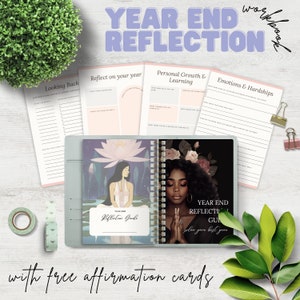 Może przedstawiać: Niebieski i biały dziennik z kwiatowym wzorem i tekstem "Year End Reflection Guide" na okładce. Dziennik jest otwarty na stronie z tekstem "Year End Reflection Guide" i kobietą o długich czarnych włosach i białej sukience. Dziennik leży na białym drewnianym blacie z zielonymi roślinami i rolką taśmy.