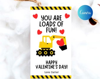 May include: A white gift tag with a yellow and black striped border. The tag features a yellow excavator holding a red heart, with the text "YOU ARE LOADS OF FUN!" and "HAPPY VALENTINE'S DAY!"