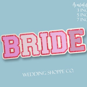 Puede incluir: Una pegatina rosa y blanca con la palabra "BRIDE" con un borde rosa brillante, sobre un fondo azul claro. La pegatina está disponible en tamaños de 7,6, 12,7 y 17,8 cm. El texto "WEDDING SHOPPE CO." está en la parte inferior.