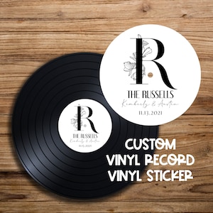 Op de afbeelding: Een witte vinyl platen sticker met een zwart bloemmotief en de letter "R" in het midden. De tekst "THE RUSSELLS Kimberly & Austin 11.13.2021" is onder het ontwerp gedrukt.