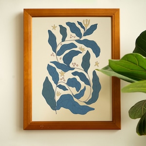 Può includere: Una stampa incorniciata di un disegno floreale blu e giallo su sfondo bianco. Il disegno presenta foglie e fiori stilizzati.