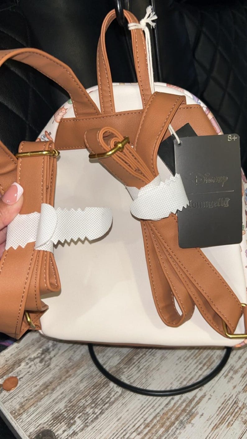 Peut inclure: Sac &agrave; dos blanc et beige avec des bretelles marron et des ferrures dor&eacute;es. Le sac &agrave; dos pr&eacute;sente un motif floral sur les c&ocirc;t&eacute;s et une &eacute;tiquette noire avec l'inscription "Disney Loungefly". Les bretelles sont r&eacute;glables.