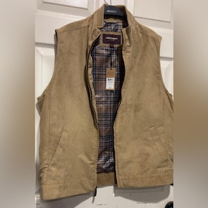 May include: A tan vest with a perforated design, a full zipper, and a plaid interior lining. The vest has a stand-up collar and a tag attached. The brand name "JOHNSTON & MURPHY" is visible on the tag.