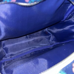 May include: A blue cosmetic bag with a white zip and a Stitch character pattern. The interior is a solid blue colour. The bag is designed to hold makeup and other beauty products.