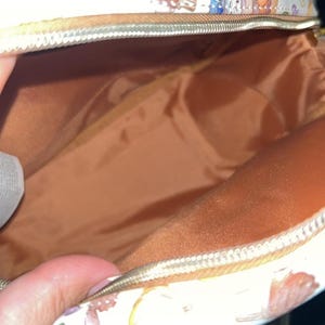 Peut inclure: Sac cosm&eacute;tique blanc ouvert avec fermeture &eacute;clair dor&eacute;e. L'ext&eacute;rieur pr&eacute;sente un motif r&eacute;p&eacute;t&eacute; de personnages de dessins anim&eacute;s, de citrouilles et d'aliments d'automne. L'int&eacute;rieur est de couleur marron uni.