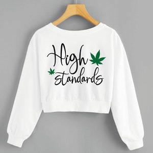 Peut inclure: Sweat-shirt blanc court avec le texte "High standards" et un graphique de feuille de marijuana verte.