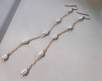 May include: A pair of long gold chain earrings with small white pearl accents.