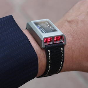 May include: A silver wristwatch with a black leather strap and a red digital display showing the time 20:02.