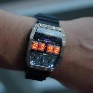 May include: A digital wristwatch with a rectangular stainless steel case and a black rubber strap. The watch face shows the time in orange numerals: 03:92. The watch has a circuit board design visible beneath the display. The strap is approximately 20 cm in length.
