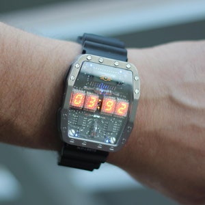 May include: A futuristic wristwatch with a silver case and a black rubber strap. The watch face displays the time in bright orange digital numbers. The watch is worn on a wrist.