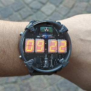 May include: A black digital wristwatch with a red LED display showing the time 09:28. The watch has a complex design with multiple buttons and a circular face.