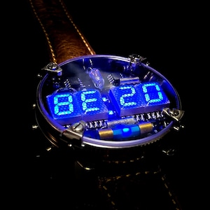 May include: A clear, round watch face with a blue digital display showing the time 08:20. The watch face is surrounded by a silver metal casing and a brown leather strap.