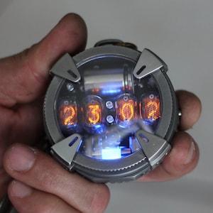 May include: A silver pocket watch with a clear face and orange glowing numbers. The watch has a round face and a silver metal casing.