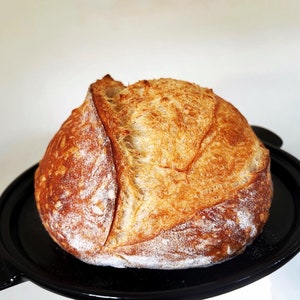 May include: A freshly baked loaf of sourdough bread with a golden brown crust and a soft, fluffy interior. The bread is sitting on a black plate.