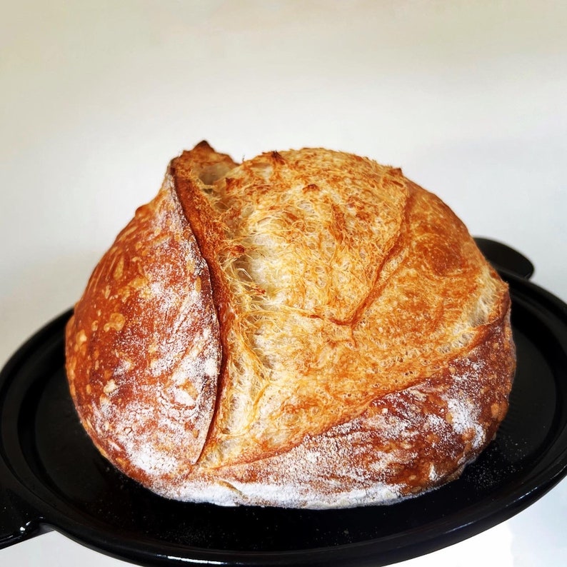 May include: A freshly baked loaf of sourdough bread with a golden brown crust and a soft, fluffy interior. The bread is sitting on a black plate.