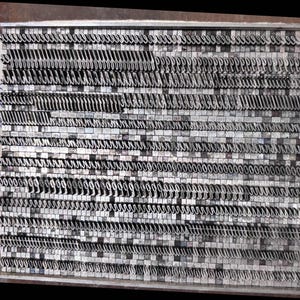 May include: A rectangular metal letterpress type tray filled with rows of silver-colored metal type characters in a script font. A white paper label attached to the side features the handwritten blue ink text 240 Repro Script.