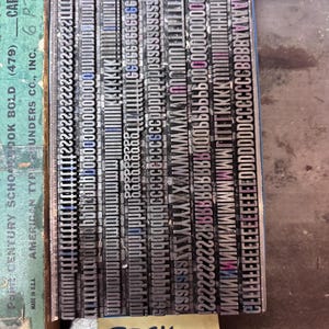 May include: A collection of metal letterpress type blocks arranged in rows within a box. The box label reads American Type Founders Co., Inc. Century Schoolbook Bold 6 Pt. A yellow sticky note at the bottom displays the handwritten text Etsy Alt Goth 1.