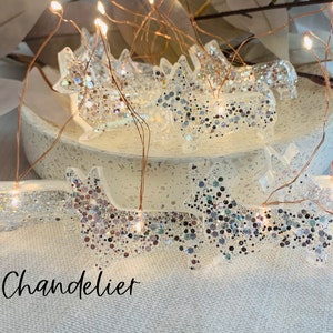 May include: A string of fairy lights with clear, glitter-covered dog-shaped ornaments. The lights are strung on copper wire and have warm white LED bulbs. The word "Chandelier" is written in cursive at the bottom of the image.
