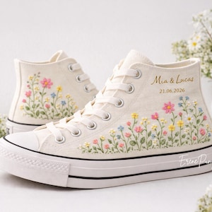 Puede incluir: Zapatillas altas color crema con bordados florales rosas, amarillos y azules. Las zapatillas tienen cordones blancos, puntera de goma blanca y una franja negra en la suela. El texto dice "Mia & Lucas" y "21.06.2026".