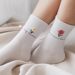 May include: White socks with embroidered floral designs. One sock features a yellow daisy, the other a red flower. Both socks have the phrase "my summer love" embroidered in cursive script.