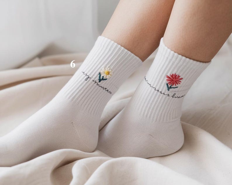 May include: White socks with embroidered floral designs. One sock features a yellow daisy, the other a red flower. Both socks have the phrase "my summer love" embroidered in cursive script.