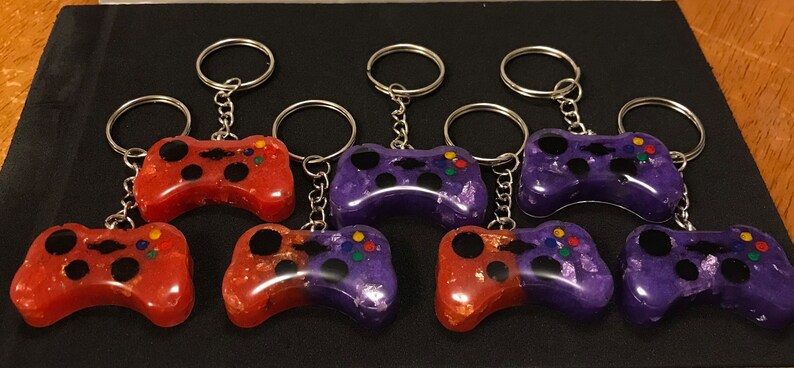 May include: Eight colorful game controller keychains, half red and half purple with black buttons, attached to silver key rings.