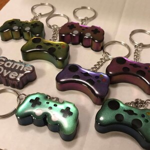 May include: Seven iridescent keychains shaped like video game controllers. One keychain has a black and white "Game Over" inscription.