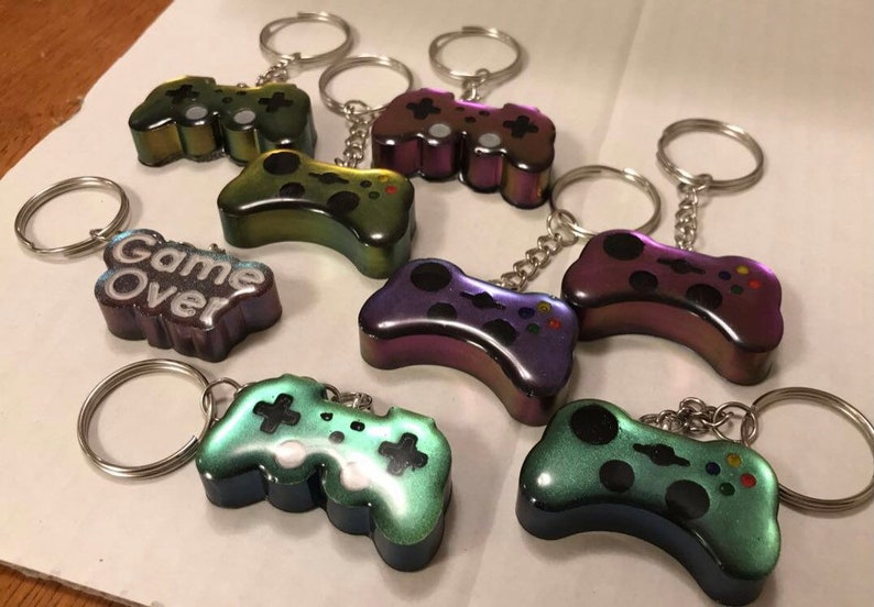 May include: Seven iridescent keychains shaped like video game controllers. One keychain has a black and white "Game Over" inscription.