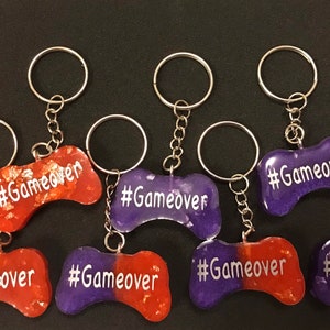 May include: Eight purple and orange resin keychains shaped like a video game controller with the text "#Gameover" on each keychain.