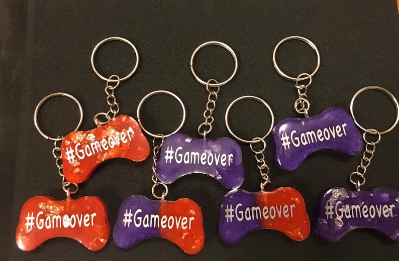 May include: Eight purple and orange resin keychains shaped like a video game controller with the text "#Gameover" on each keychain.
