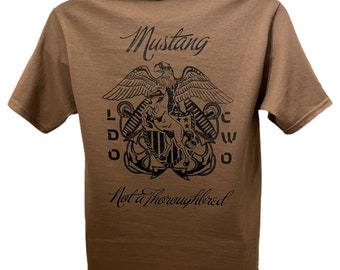 Puede incluir: Una camiseta marrón con un gráfico negro de un águila sosteniendo un caballo con el texto "Mustang" y "Not a Thoroughbred" impreso en la espalda.