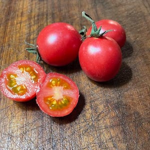 Peut inclure: Quatre tomates rouges, deux entières et deux coupées en deux, sur une surface en bois. Les tomates sont d'une couleur rouge vif et ont une finition brillante.