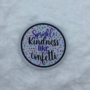 May include: A white round sticker with a black border and colorful confetti. The sticker has the text "Sprinkle Kindness like confetti" in purple and black lettering.
