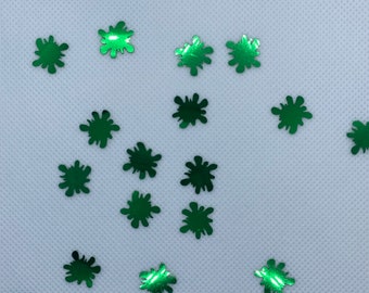 May include: Green glitter confetti in the shape of a splatter or paint drop on a white background.