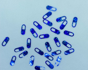 May include: A scattering of blue glitter pill shaped confetti on a white background.