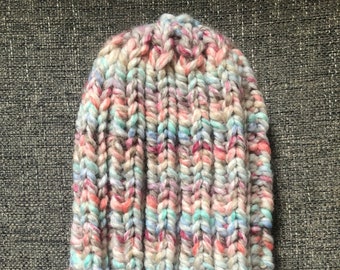 May include: A colorful knitted beanie hat with a multi-colored yarn in shades of pink, blue, and white.