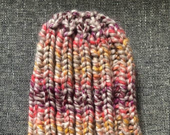 May include: A colorful knitted beanie hat with a textured pattern. The hat is made with a blend of pink, purple, orange, and beige yarn.