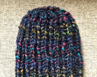 May include: A dark blue knitted beanie with a multi-colored flecked yarn. The beanie is made with a chunky yarn and has a ribbed texture.