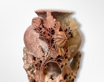 May include: A small, intricately carved stone vase with a reddish-brown hue. The vase features a floral design with leaves and buds, and a base with a decorative, swirling pattern.
