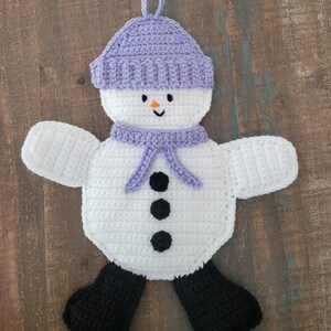 Puede incluir: Un adorno de muñeco de nieve tejido a crochet con un gorro y una bufanda morados. El muñeco de nieve tiene ojos y botones negros y una pequeña nariz naranja. El texto "Light Jasmine" está escrito debajo del muñeco de nieve.