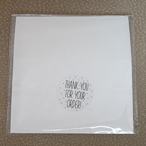 Puede incluir: Tarjeta blanca con una pegatina en blanco y negro que dice "&iexcl;Gracias por tu pedido!"