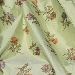 May include: A light green fabric with a floral pattern. The flowers are in shades of orange, blue, and green.
