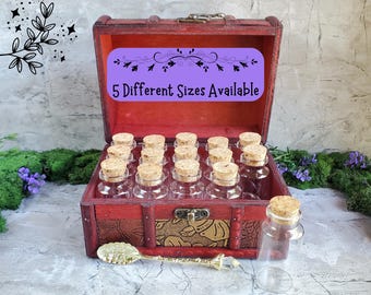 May include: A red wooden chest with a metal latch containing multiple clear glass bottles with cork stoppers. A purple label inside reads 5 Different Sizes Available. A small gold-toned spoon with a crystal-like handle rests in front.