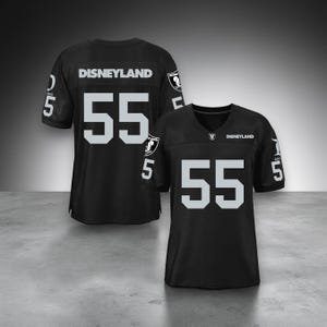 May include: A black athletic jersey featuring the text Disneyland and the number 55 in large white font on the front and back. The sleeves display the number 55 and a circular logo with a Mickey Mouse silhouette. The jersey has a V-neck collar.
